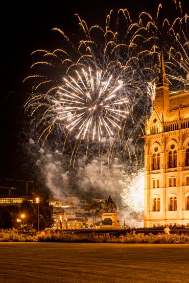 Fireworks illuminate the night sky over a historic building and statue.