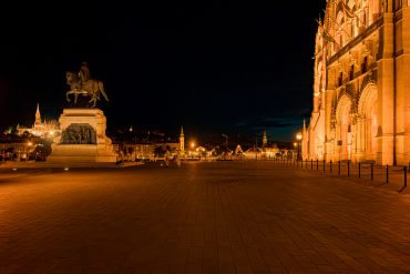 Night view of a statue and illuminated historic building in a city square.