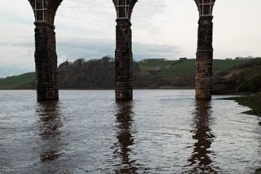 Stone arches of a viaduct over a calm river reflecting pillars in water.