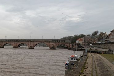 A stone bridge over a river with boats docked along the walkway.
