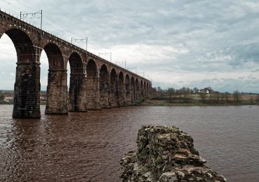 Stone arch railway bridge over a river on a cloudy day.