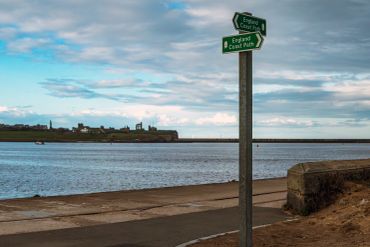 Signpost showing directions for the England Coast Path by the water.