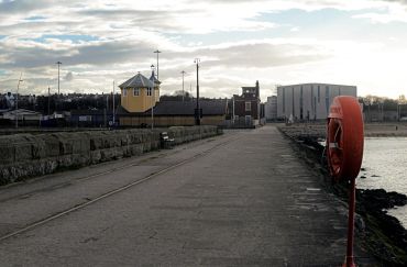 A coastal pathway with a yellow building and a life buoy on the right.