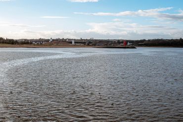 Coastal town with a distinctive red lighthouse on the shore under a partly cloudy sky.