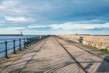 Pier walkway with railings, two distant lighthouses, and a partly cloudy sky.