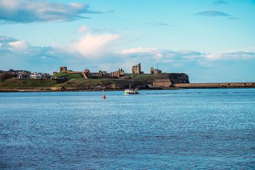 Fishing boat near a coastal town with historic ruins under a blue sky.