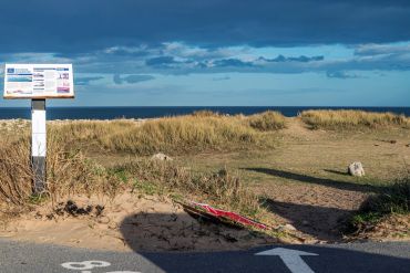 Information board near coastal dunes under a cloudy sky.