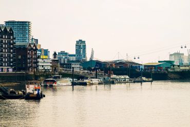 A waterfront cityscape with boats and modern buildings under a pale sky.