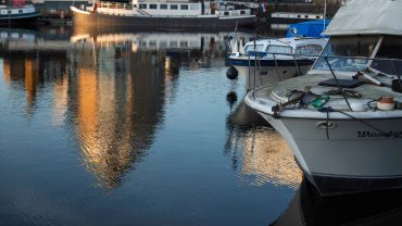 Boats docked on calm water with city reflections at sunset.
