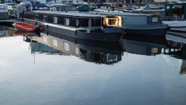 A sleek black narrowboat docked with a small orange dinghy beside it.