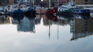 Several boats docked peacefully in an urban harbor with reflections on the water.