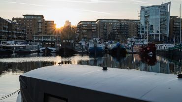 Boats docked in a marina with sunset behind urban buildings.