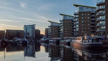 Modern waterfront apartments and boats at sunset with reflections on the water.