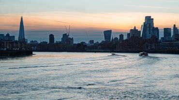 Sunset over the London skyline with boats on the Thames River.