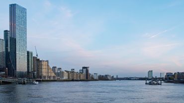Modern city skyline along a river at dusk.