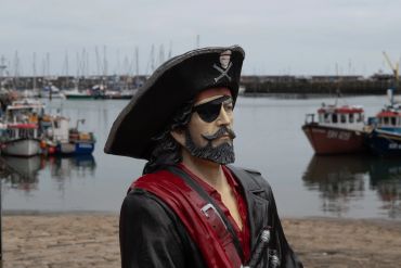 Statue of a pirate by a harbor with boats in the background.