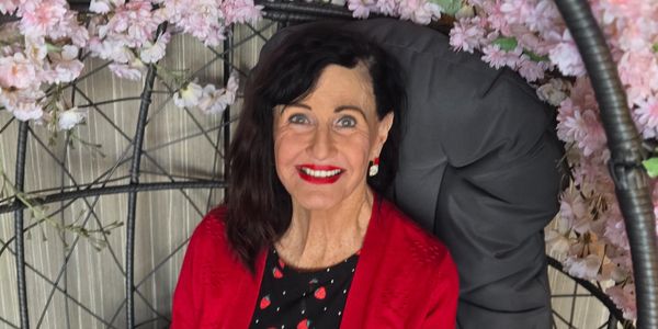 Smiling woman in red cardigan sitting in a floral-decorated chair.
