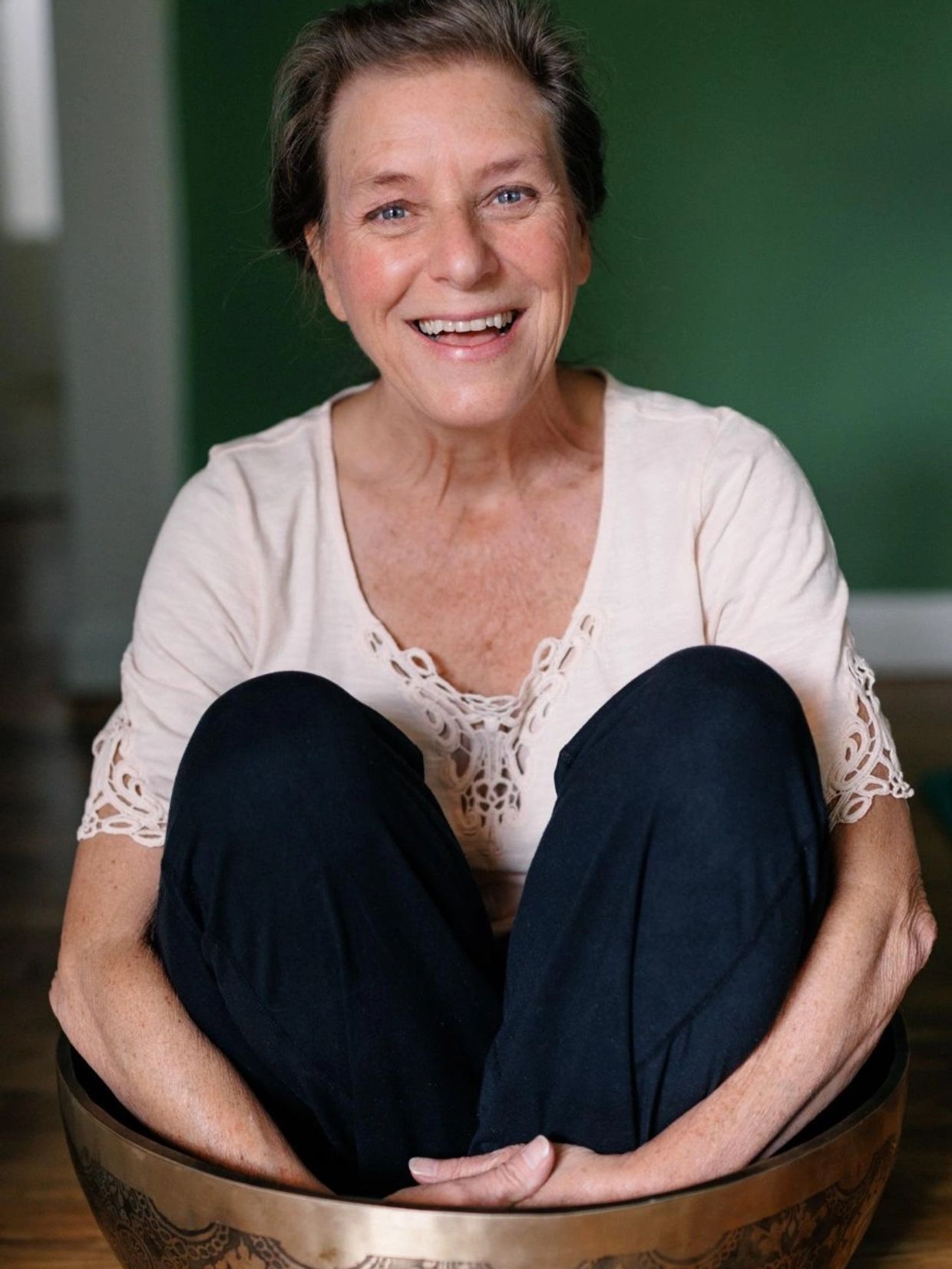 Smiling older woman sitting in a large brass bowl.
