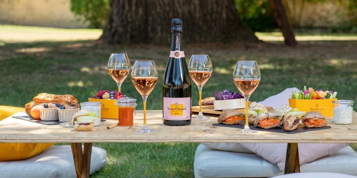 Outdoor picnic table with champagne, glasses, and assorted appetizers.