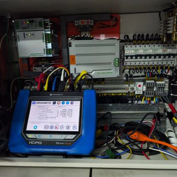 An electrical testing device connected to a control panel with various wires and components.