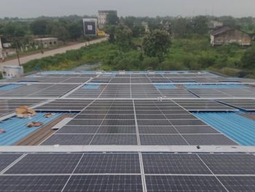 Solar panels installed on a large rooftop in a green area.