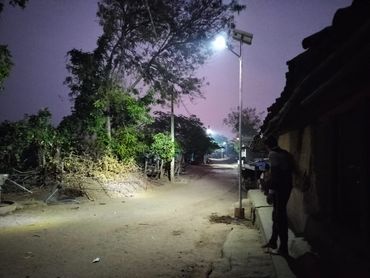 A person standing near a dimly lit rural street at dusk.