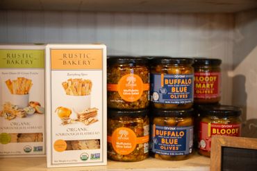 Organic sourdough flatbread and jars of olive salad and stuffed olives on a shelf.