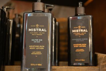 Two bottles of Mistral moisture-rich body lotion for men on a wooden shelf.