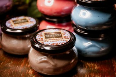 Colorful candles in decorative jars with black lids on a wooden surface.