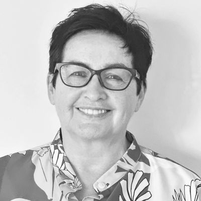 Smiling woman with glasses wearing a patterned shirt against a plain background.