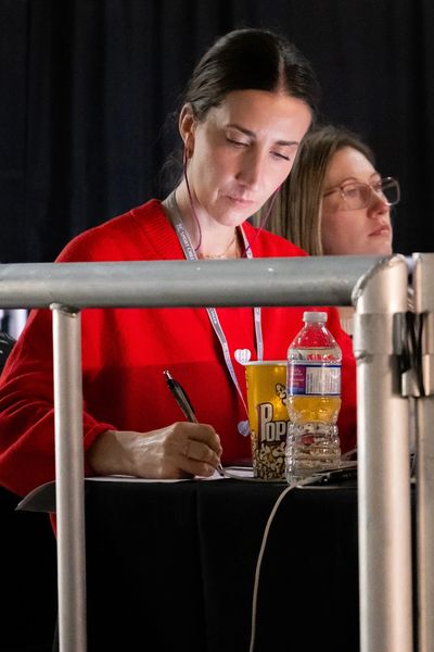 A woman in a red sweater writing at a table with popcorn and water bottle nearby.