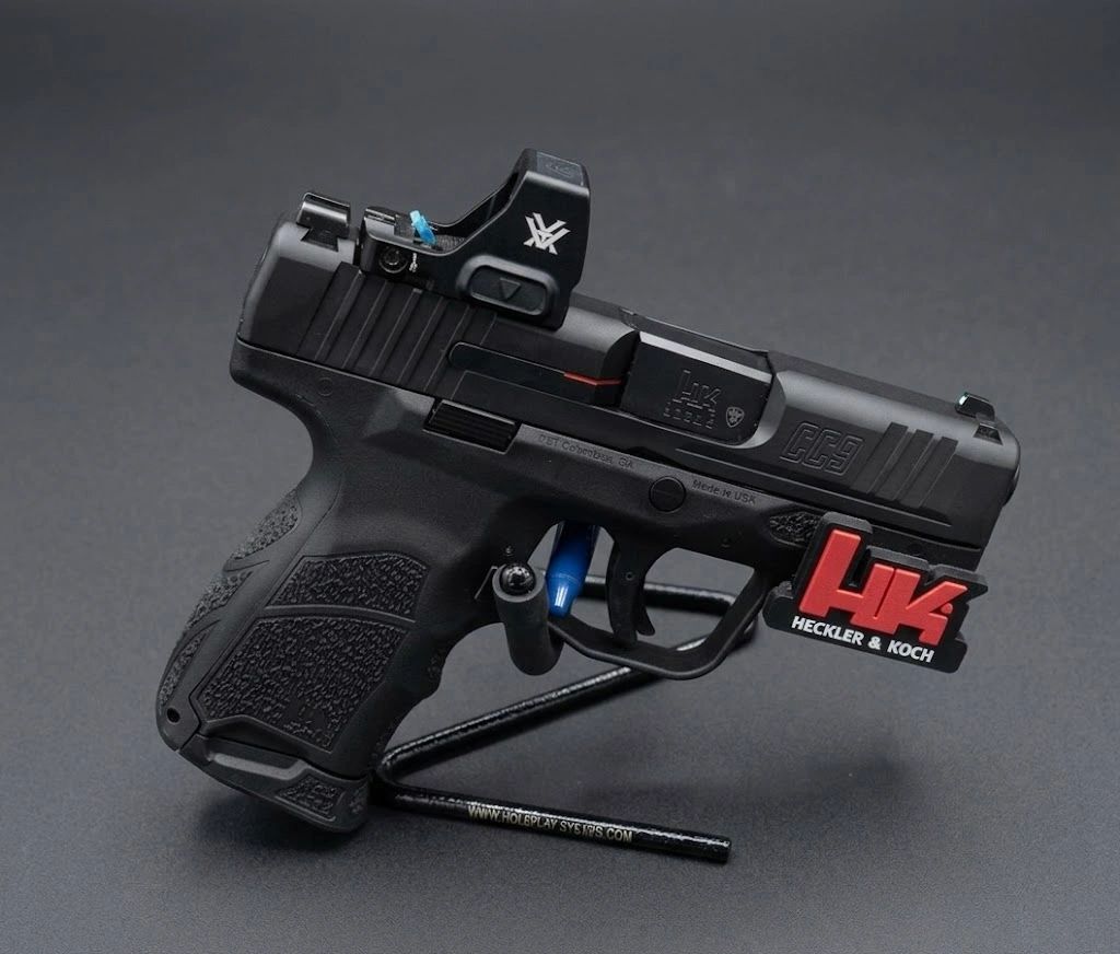 Heckler & Koch firearm with red dot sight on display stand.