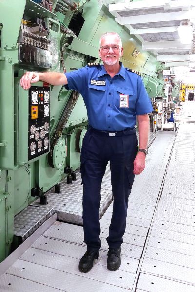 Man in blue uniform standing in an engine room.