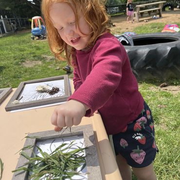 A young girl creating art with grass outdoors on a sunny day.
