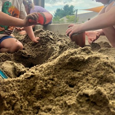 Children playing and digging in a large sandbox outdoors.