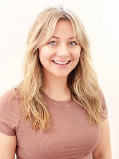 Smiling blonde woman with wavy hair wearing a mauve top.