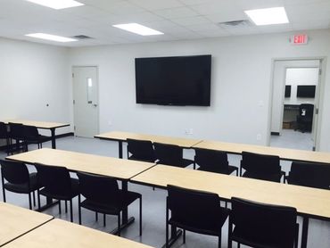 Chairs set up at tables in front of a television set in a classroom.
