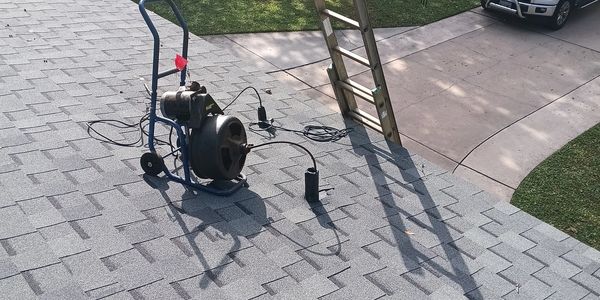A roofing tool and ladder casting shadows on a shingled roof under sunlight.
