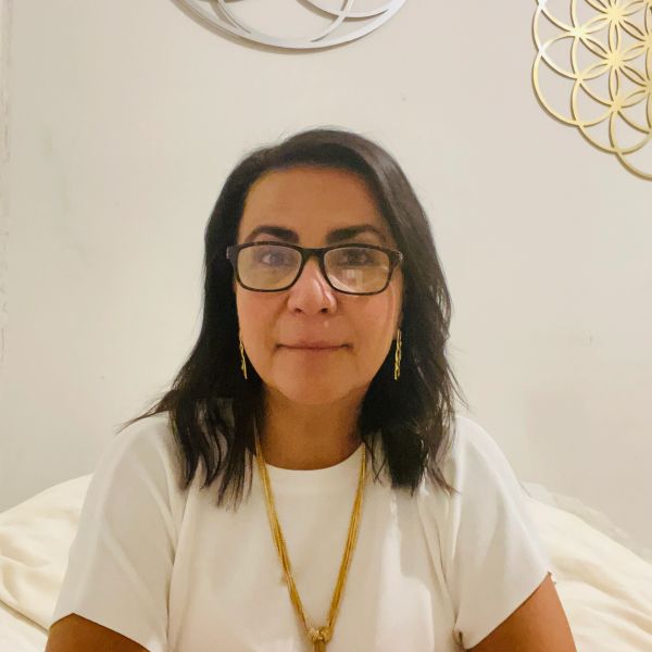 Mujer con gafas y collar dorado, vestida de blanco.