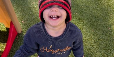 Child wearing a hat and sweater smiling outdoors.
