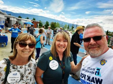 Three adults smiling at a community event outdoors.