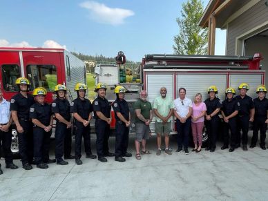 Group photo of firefighters and civilians in front of fire trucks.