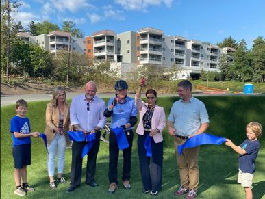 Group cutting a blue ribbon outdoors during a ceremony.