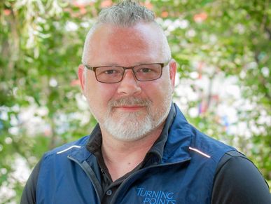 Smiling man with glasses and white beard outdoors.