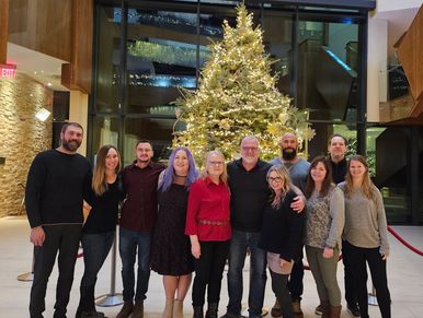 Group of people posing indoors in front of a decorated Christmas tree.