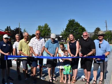 Group cutting ribbon at outdoor event on sunny day.