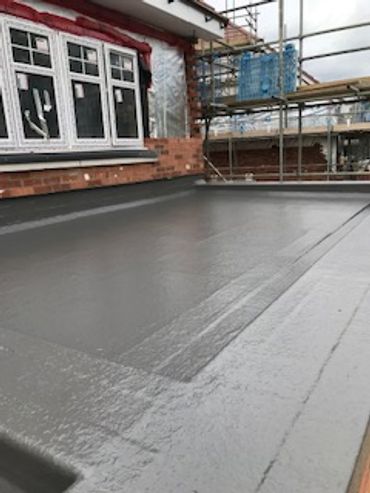 Newly installed flat roof with waterproof membrane near a brick house under construction.