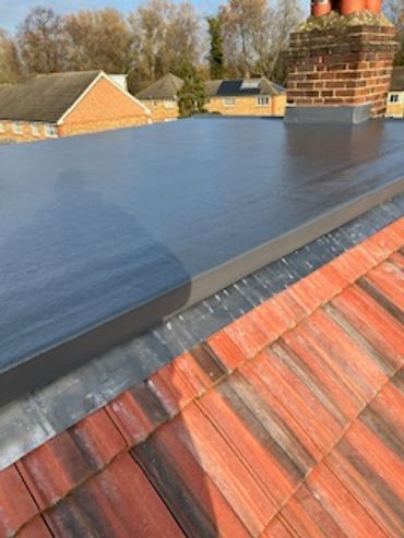A flat roof with a smooth, dark waterproof surface above red roof tiles.