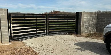 Modern black metal gate between two concrete block pillars.