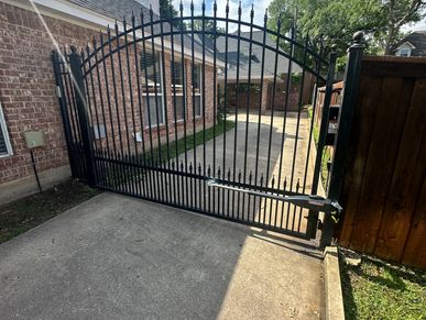 Wrought iron gate with brick wall and concrete driveway.